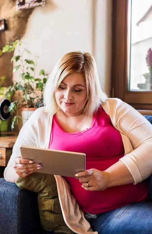 A Woman Lays on Her Couch Reading a Tablet with a Smile on Her Face.