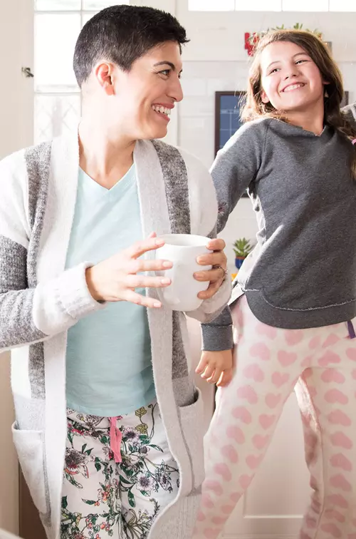 A woman dancing in the kitchen with her daughters and drinking coffee.