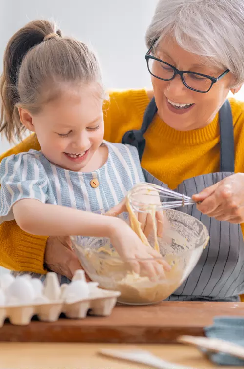 A Grandmother and Granddaughter Mix Cookie Dough Ingredients in the Kitchen