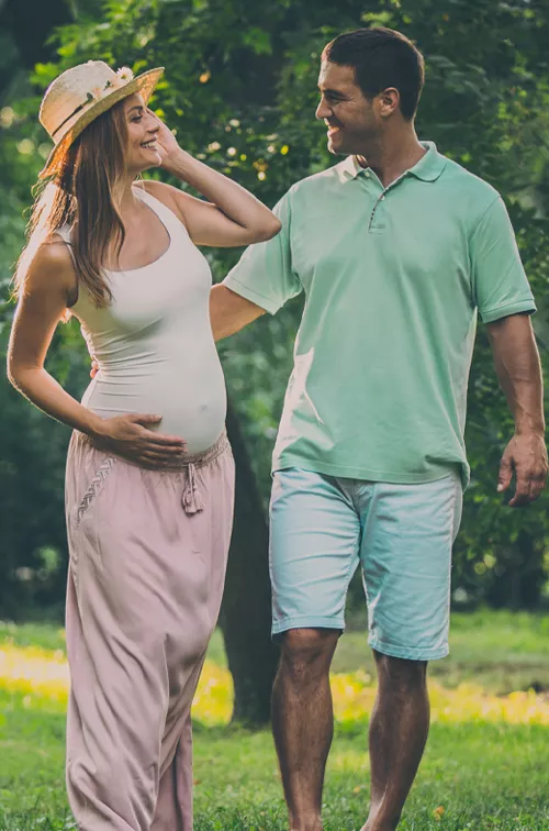 A pregnant woman walking outdoors with her husband.