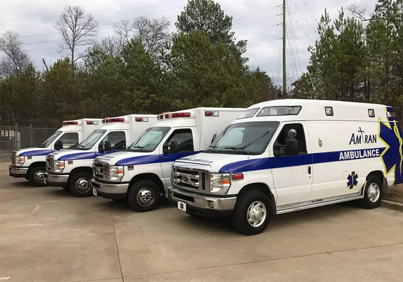 Four medical transport vans with the words Amtran sit in a parking lot