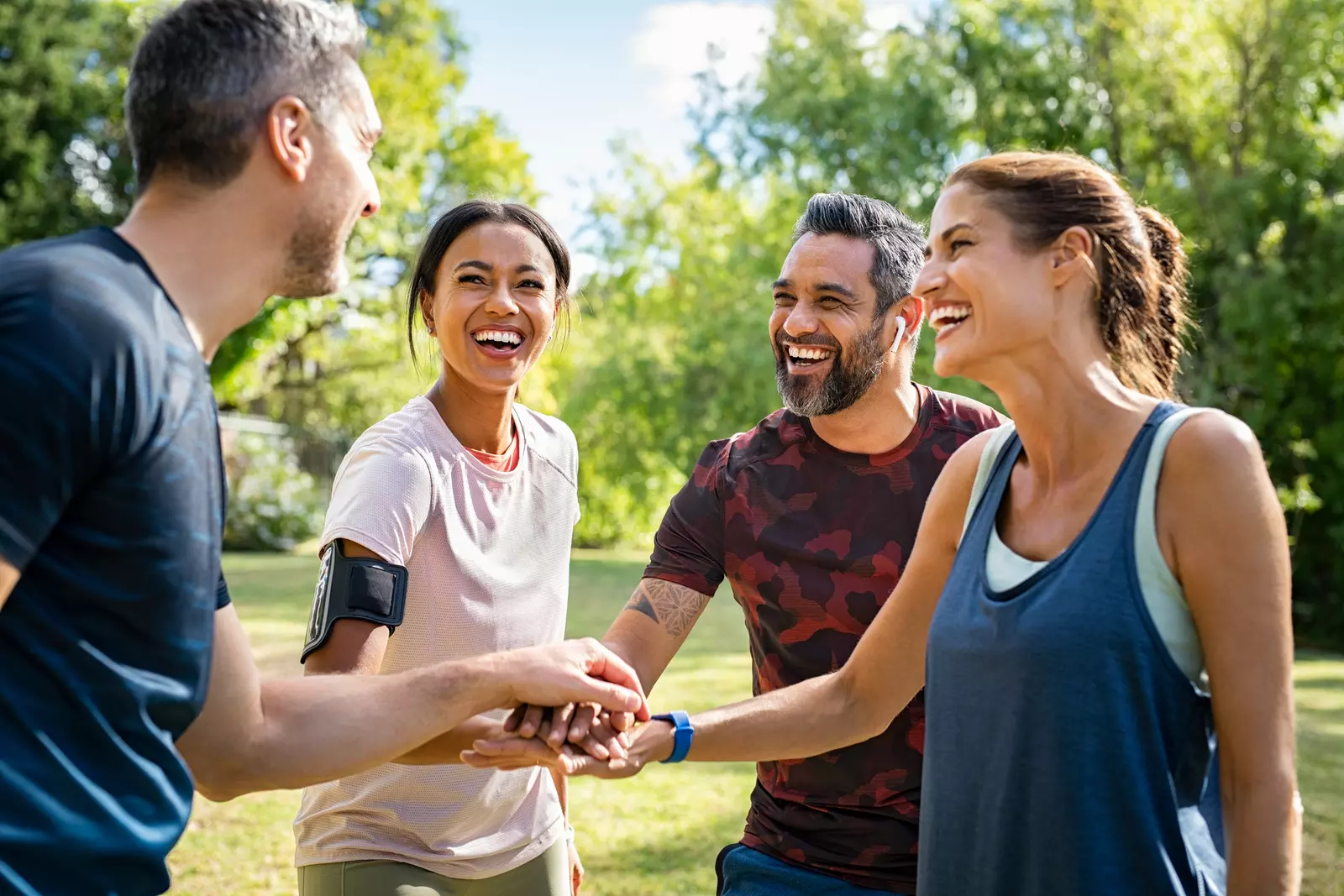 Group of active mature friends in park stacking hands after workout - stock photo