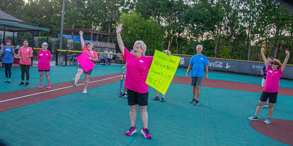 woman in pink holds up sign and cheers for kickball team
